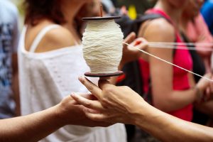 Deux mains se passent une bobine de fil blanc au milieu des spectateurs — Fibre