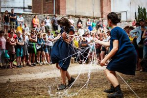 Deux danseuses tirent un écheveau de fils blancs devant le public, dans une cour — Fibre