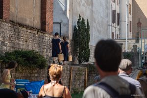 Deux danseuses gravissent un escalier de pierre, sacs de toile à la main, vues depuis le public — Fibre