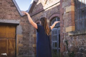 Danseuse de dos, bras levés, devant un bâtiment industriel en brique — Fibre
