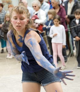 Danseuse aux bras couverts de traces bleues, mains tendues, devant le public d'une rue — Fibre