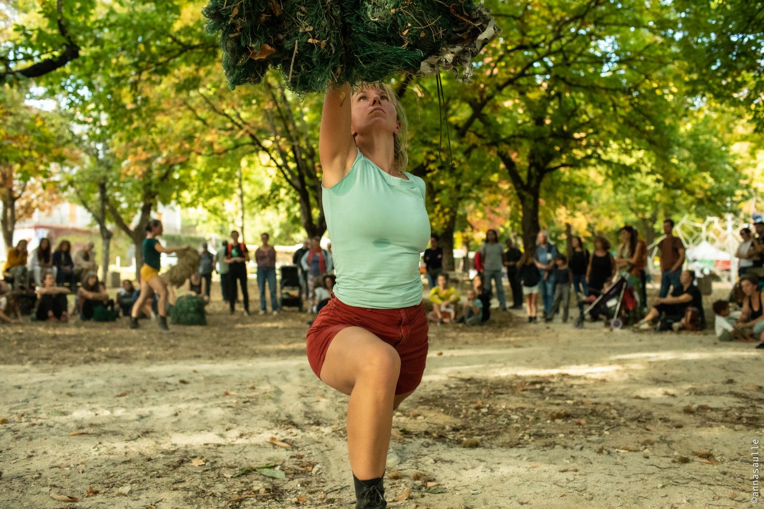 Danseuse soulevant à bout de bras une masse de filet végétal, devant le public dans un parc — Hors Sol
