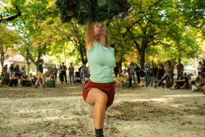 Danseuse soulevant à bout de bras une masse de filet végétal, devant le public dans un parc — Hors Sol