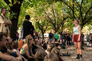Danseuse debout face au public assis dans l'herbe sous les arbres — Hors Sol