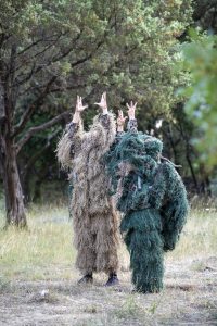 Deux interprètes en costumes de fibres beige et vert, mains dressées au-dessus de la tête, dans la garrigue — Hors Sol