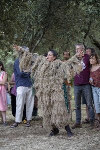 Interprète en costume de fibres beige, bras tendus de part et d'autre, au milieu du public — Hors Sol