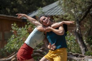 Duo de danseuses joue contre joue, bras déployés, devant une bâtisse de garrigue — Hors Sol