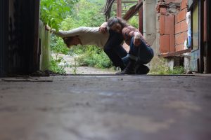 Danseuse portée à l'horizontale par sa partenaire accroupie, dans un passage extérieur délabré — Hors Sol
