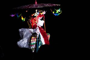 Silhouette sous une ombrelle constellée de grues en origami, sur scène noire — Kimonoshima